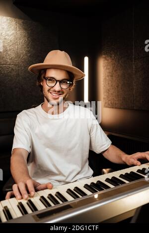 Giovane arrangiatore di musica di stile che compone la canzone sul pianoforte midi in studio di registrazione. Un ragazzo attraente che gioca felicemente al pianoforte elettrico in uno studio moderno Foto Stock