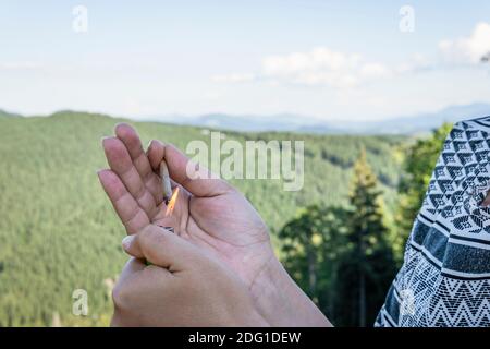 Primo piano della mano femminile illumina la giuntura di marijuana all'aperto. Canapa smussata nella mano femminile. La cannabis è un concetto di erbe e medicina alternativa Foto Stock