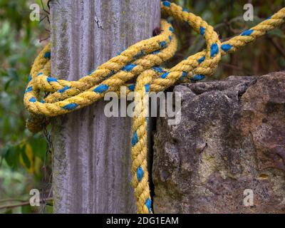 Fotografia ravvicinata di una corda di nylon giallo e blu legata ad un palo di legno, catturata in una casa vicino alla città coloniale di Villa de Leyva Foto Stock