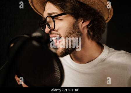 Primo piano bel musicista maschile cantando emotivamente in registrazione microfono canzone in studio audio professionale Foto Stock