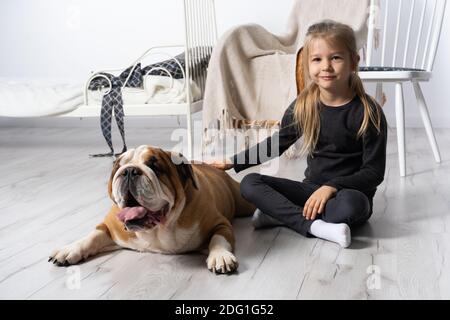 La bambina sta accarezzando il cane. Bulldog inglese come fedele amico dell'uomo. Una razza con un cappotto marrone con macchie bianche. Foto Stock