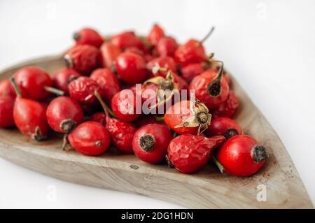 Bacche di roseanca in una ciotola di legno su uno sfondo chiaro primo piano. Frutti di bosco per la preparazione di tè o bevande vitaminici. Foto Stock