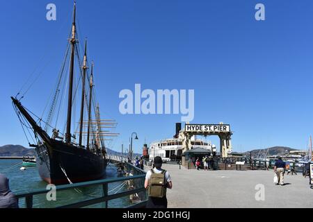 Hyde Street Pier, parte del San Fransisco Maritime National Historic Park. Una goletta è ormeggiata al molo e i turisti camminano intorno alle attrazioni. Foto Stock