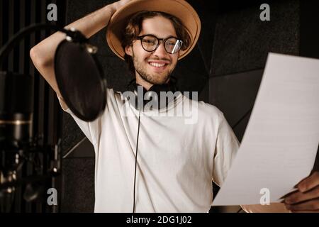 Ritratto di giovane cantante maschile sorridente felice di leggere il testo di nuovo brano in studio di registrazione Foto Stock