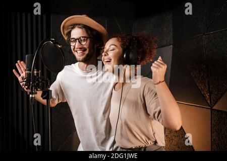 Giovani musicisti attraenti cantano felicemente insieme registrando una nuova canzone in studio audio Foto Stock