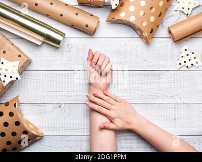 Scatole regalo di Natale e carta da imballaggio in colori oro su sfondo di legno bianco. Copiare spazio per il testo. Disposizione piatta e vista dall'alto. Mani femminili Foto Stock