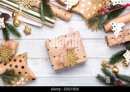 Scatole regalo di Natale e carta da imballaggio in colori oro su sfondo di legno bianco. Copiare spazio per il testo. Disposizione piatta e vista dall'alto Foto Stock