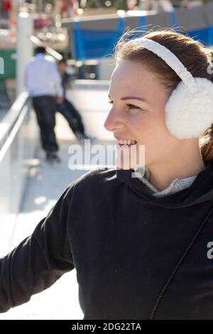 Bruna giovane donna con Earflaps sorridere mentre sulla pista di pattinaggio su ghiaccio Foto Stock