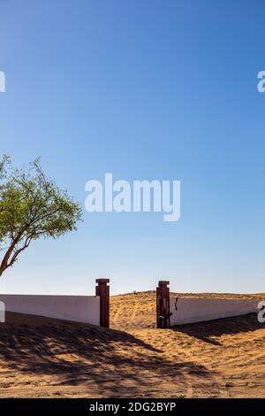 Villaggio fantasma di al Madam, cortile abbandonato e recinzione in mattoni con cancello d'ingresso sepolto nella sabbia a Sharjah, Emirati Arabi Uniti. Foto Stock