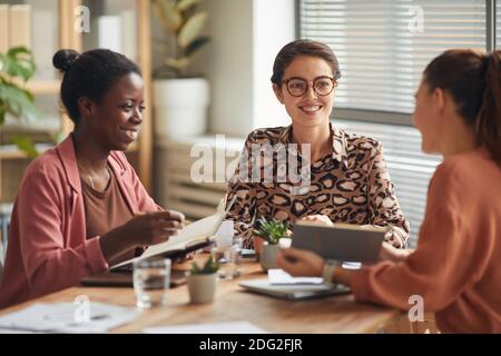 Ritratto di una squadra di lavoro femminile di successo che discute il lavoro durante la riunione tavolo e sorridente allegro Foto Stock