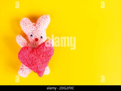 Biglietto festivo per il giorno di San Valentino con un coniglietto giocattolo fatto a mano e un cuore decorativo. Foto Stock