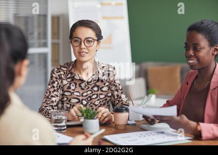 Ritratto di giovane donna d'affari che indossa occhiali mentre conduce incontro con team aziendale femminile in ufficio Foto Stock