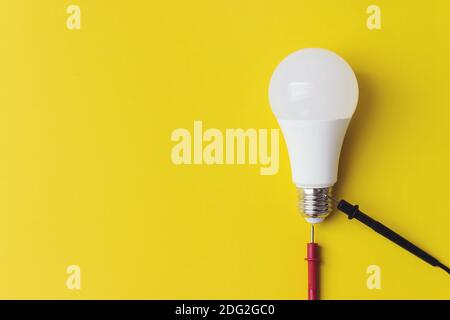 Lampadina incandescente con sonde del multimetro su sfondo giallo, concetto di unicità. Idea, innovazione, concetto di creatività, Foto Stock