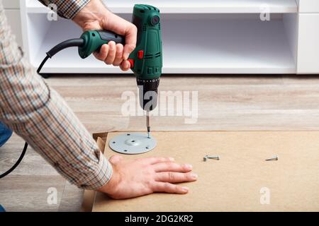 Processo di assemblaggio dei mobili, master raccoglie i mobili da tavolo utilizzando uno strumento di perforazione. Movimento, miglioramento della casa, ristrutturazione di riparazione di mobili Foto Stock