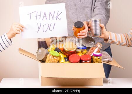 I volontari raccolgono i prodotti alimentari nella scatola di donazione e nella custodia Foglio di carta con messaggio grazie Foto Stock