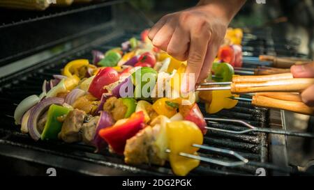 Mano dell'uomo con griglia per barbecue. Cuocete uno spiedino delizioso sulla carne alla griglia. Cibo cucinato con barbecue alla griglia. Chef cucina brochette in cortile di un hous Foto Stock