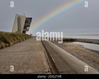 Rainbow at Rossall Beach, Fleetwood, Lancashire, Regno Unito. L'edificio a quattro piani sul lungomare esterno di Rossall Point e' la Torre dell'Orologio costiero di Rossall. Foto Stock