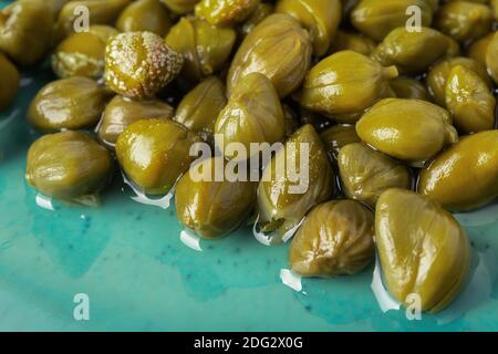Primo piano di capperi decapati su un piatto turchese. Gemme marinate di cappero cespuglio. Ingredienti della cucina mediterranea. Spezie e condimenti biologici. Foto Stock