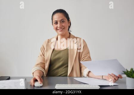 Ritratto di giovane donna di razza mista sorridente mentre si usa il PC alla scrivania, concetto di riunione online, POV Foto Stock
