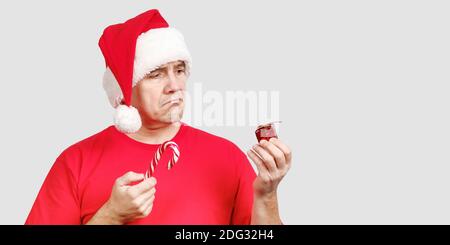 Uomo in cappello di Santa con canna caramella in mano Contiene il piccolo regalo di Natale difettoso Foto Stock