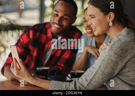 Amici che guardano le foto sul telefono cellulare. Gruppo di giovani seduti al tavolo da caffè e guardando il telefono cellulare. Foto Stock