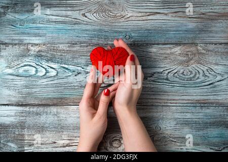 Cuore rosso fatto di filo nelle mani delle donne su uno sfondo di legno. Foto Stock