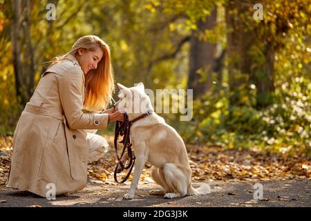 donna e simpatico cane nella foresta, bionda caucasica femmina in mantello tra foglie caduti al sole giorno d'autunno Foto Stock