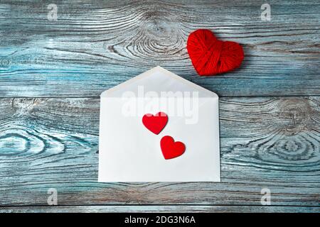 Busta bianca e cuori rossi su sfondo di legno blu-grigio. Foto Stock