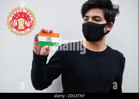 L'uomo indiano indossa tutta la maschera nera e facciale, tieni la bandiera indiana in mano isolata su sfondo bianco con l'emblema di stato di Madhya Pradesh . Coronavirus India sta Foto Stock