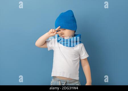 Bambino ragazzo con le dita mostra segno gesto selfie, vittoria, simbolo di pace e patsefismo. Studio in primo piano girato con cappello e snod blu a maglia calda Foto Stock