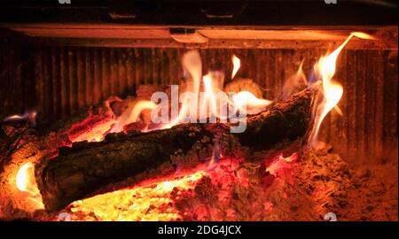 particolare dell'interno di un camino con un tronco di quercia ardente e braci rosso-caldi intorno ad esso, orizzontale Foto Stock