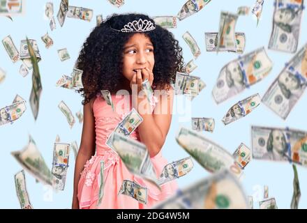 Bambino afroamericano con capelli ricci che indossano la corona della principessa cercando stressato e nervoso con le mani sulla bocca che mordicchiano i chiodi. Problema di ansia. Foto Stock