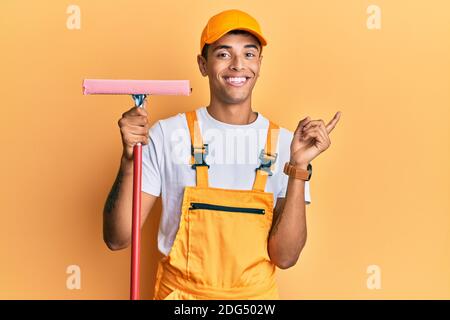 Giovane bell'afroamericano uomo detergente per vetri che tiene la rondella di vetro sorridendo felice puntando con mano e dito a lato Foto Stock