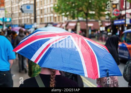 Giornata piovosa a Londra con una donna che indossa un ombrello Con la bandiera della Gran Bretagna Foto Stock