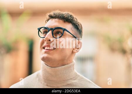 Giovane ispanico sorridente felice indossare occhiali in città. Foto Stock