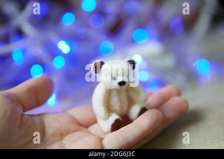 orso cucito in miniatura sul palmo della mano. Teddy orso polare sullo sfondo di blu fata luci. copyspace. Foto Stock