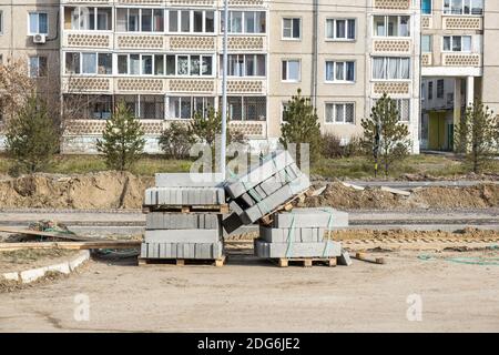 Nuovi cordoli in calcestruzzo in blocchi su pallet in legno, lavori stradali. Costruzione, riparazione di strade in zona residenziale della città. Riparazione di infrastrutture stradali. Foto Stock