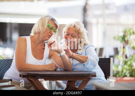 Donne mature che usano l'orologio intelligente nel caffè di strada Foto Stock