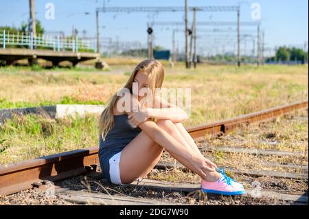 Triste giovane ragazza seduta lonely sul binario Foto Stock