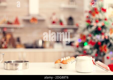 Ingredienti per la preparazione di deliziosi biscotti sul tavolo in camera vuota. Cucina il giorno di natale con nessuno in camera decorata con x-mas albero e ghirlande Foto Stock