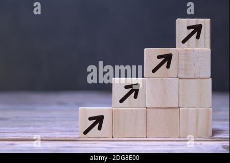 Processo di successo per la crescita del concetto aziendale. Blocchi di legno accatastati come scala con le frecce che vanno in su, isolati su uno sfondo scuro, spazio di copia. Foto Stock