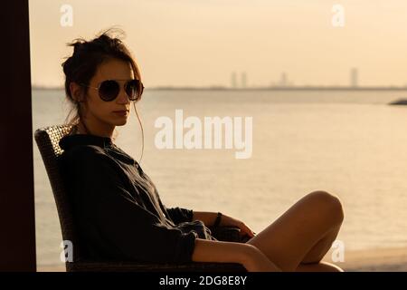 Giovane donna godendo il tramonto dalla terrazza della villa a. La spiaggia e guardando lo skyline di Abu Dhabi durante il tramonto Foto Stock