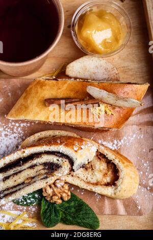 Lo strudel di papavero è decorato con zucchero in polvere, cannella, noci e menta e tè in una tazza di carta. Torta fatta in casa con ingredienti naturali. Legno rustico Foto Stock