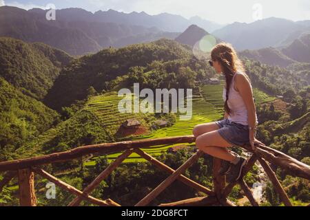 Una giovane ragazza si trova sulla rotaia di legno e si affaccia sui campi di riso verde cascate a Sapa, Vietnam Foto Stock