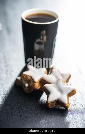 Stelle di pan di zenzero ghiacciato e tazza di caffè. Biscotti di Natale tradizionali in tavola nera. Foto Stock