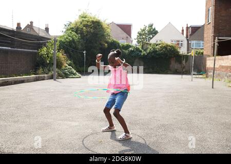 Giocosa ragazza felice che gira in cerchio di plastica in un quartiere soleggiato Foto Stock