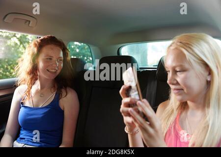 Presetare amici ragazza utilizzando smartphone nel sedile posteriore di auto Foto Stock