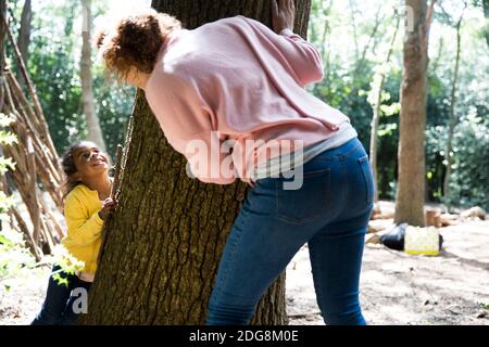 Madre e figlia che giocano nascondono e vanno a cercare l'albero tronco in legno Foto Stock