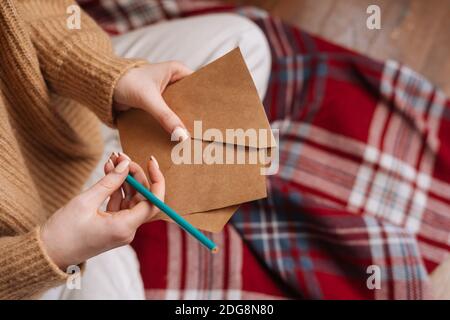 Mani ravvicinate di una giovane donna irriconoscibile che tiene una busta vuota e. penna preparazione lettera di scrittura Foto Stock