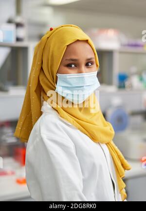 Ritratto sicuro scienziato femminile in hijab e maschera viso in laboratorio Foto Stock